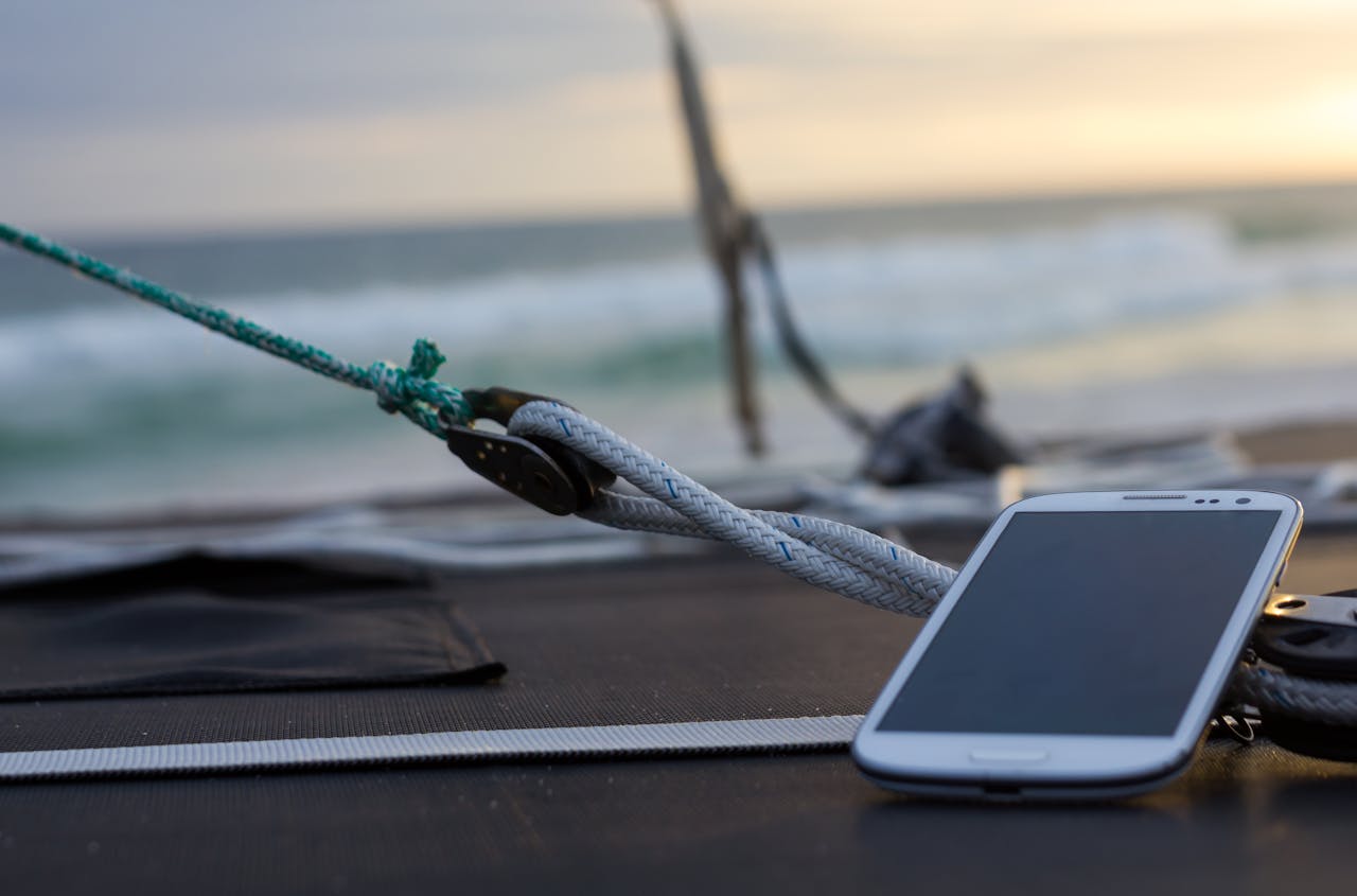 Home Close-up of a smartphone resting on a sailboat deck with the ocean waves in the background.