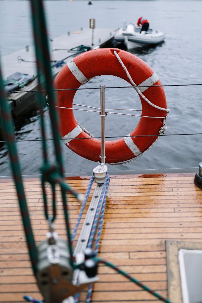 Close-up of a red lifebuoy on a wooden sailboat deck near a pier, conveying safety.