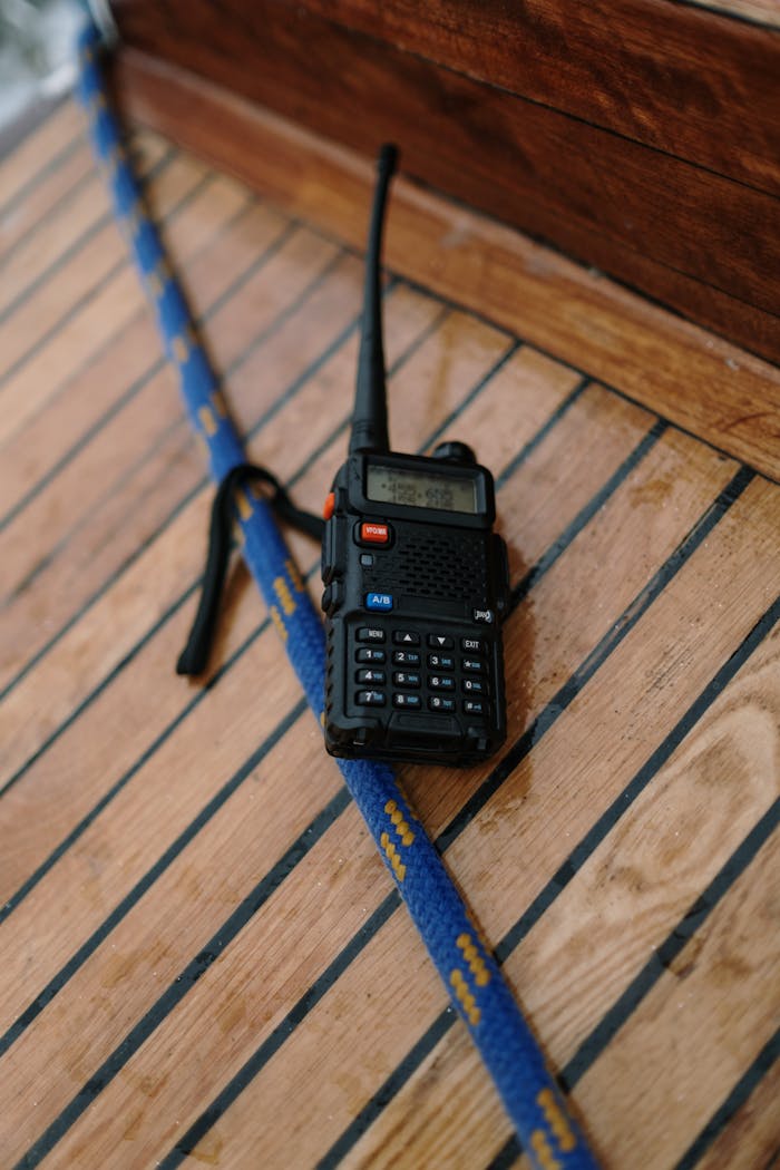 Home A two-way radio placed on a wooden surface next to a blue rope, possibly on a boat deck.